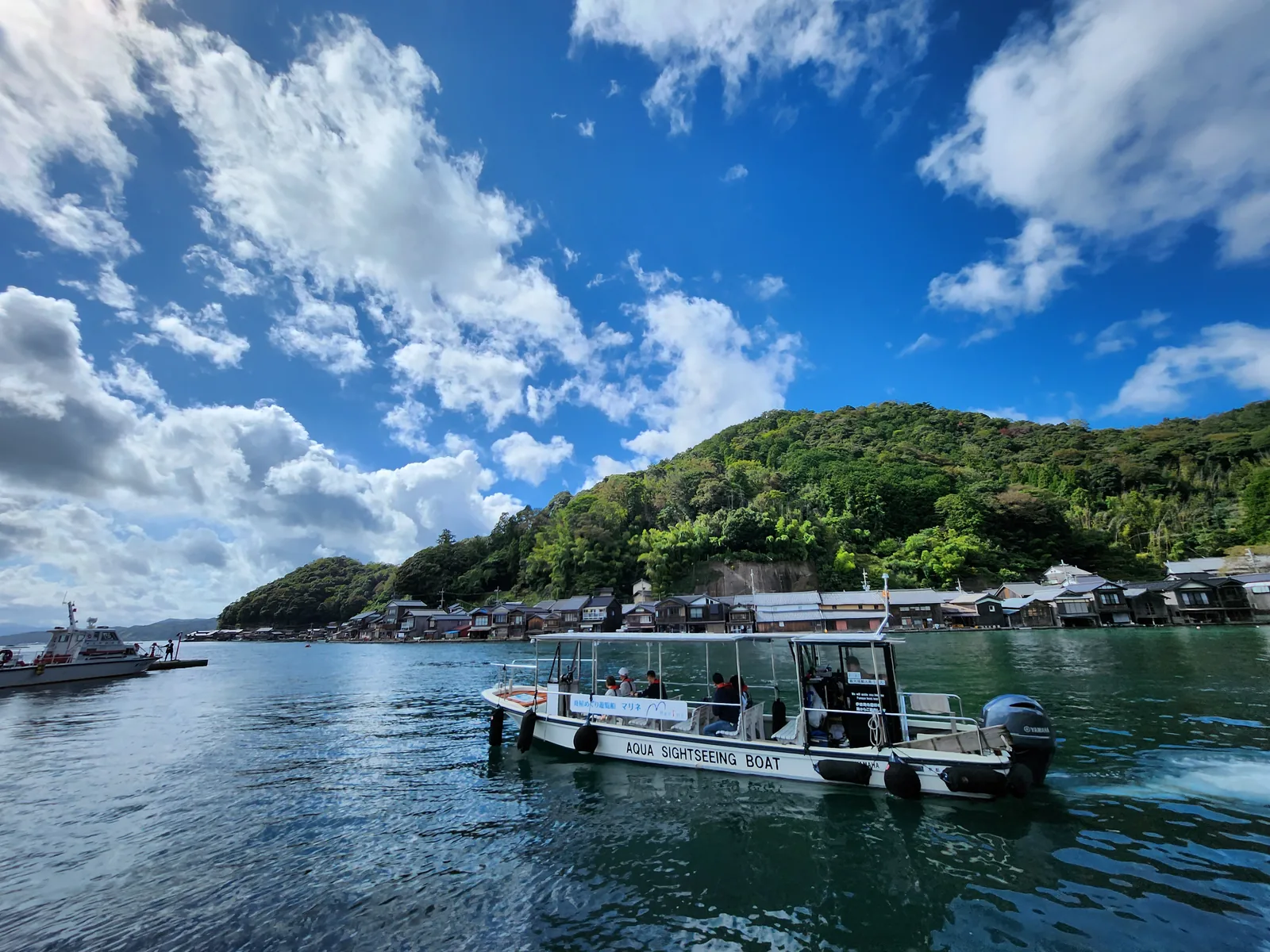 伊根灣遊覽船航行於藍色海面與舟屋聚落前