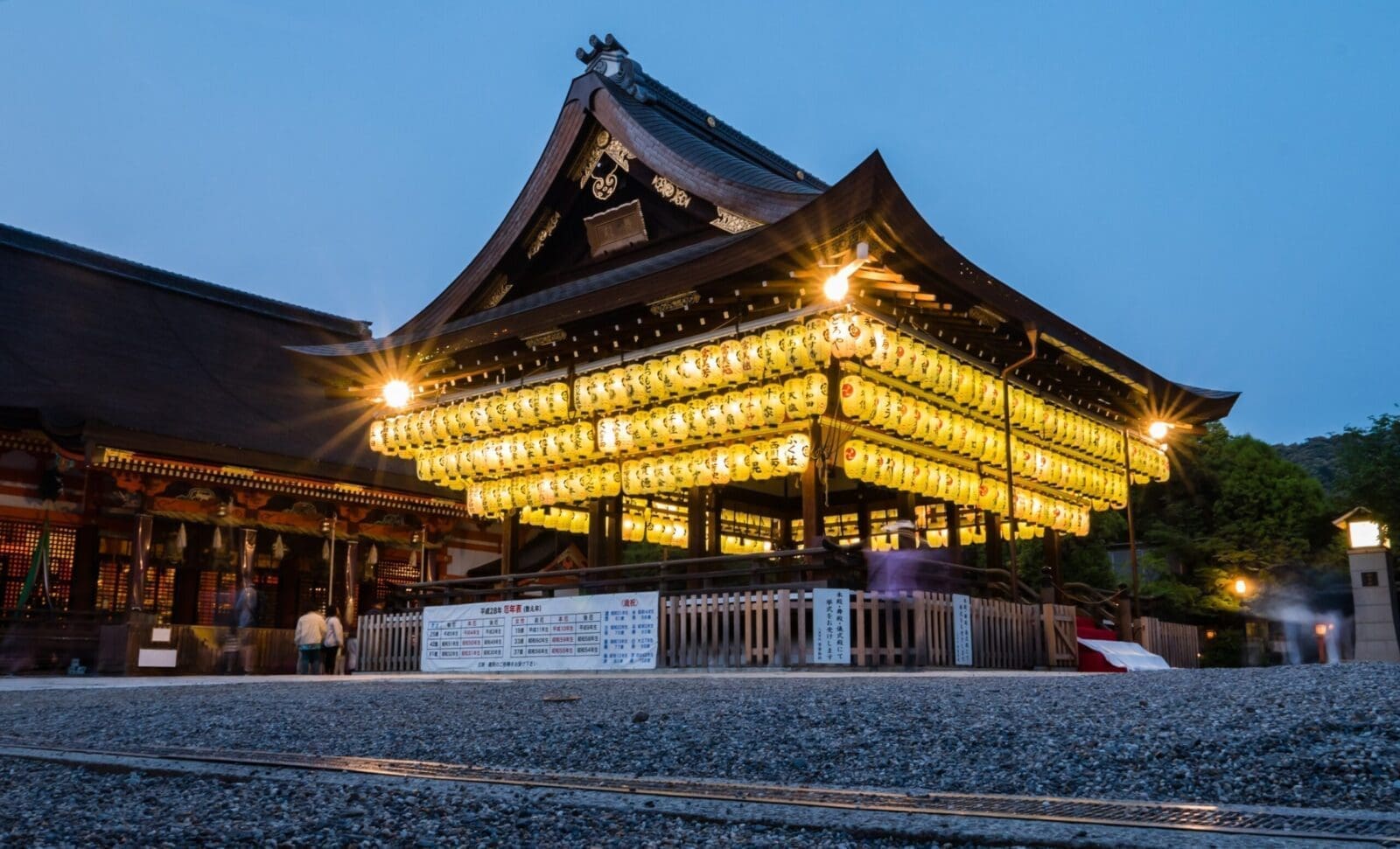 京都八坂神社舞殿在夜間點亮成排提燈，周圍有參拜旅客