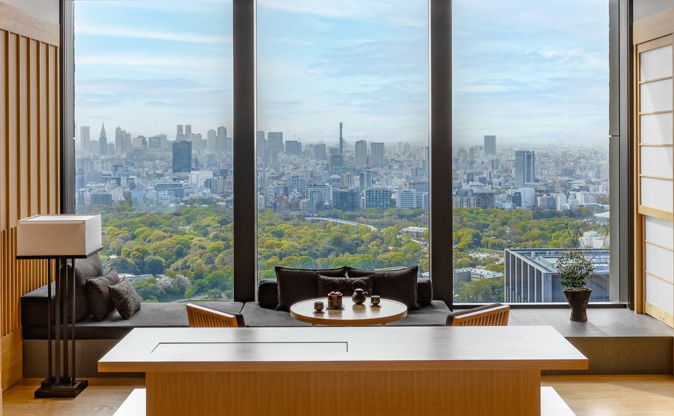 東京安縵｜客房起居區的長桌、座椅與窗外的都心綠地與大樓群