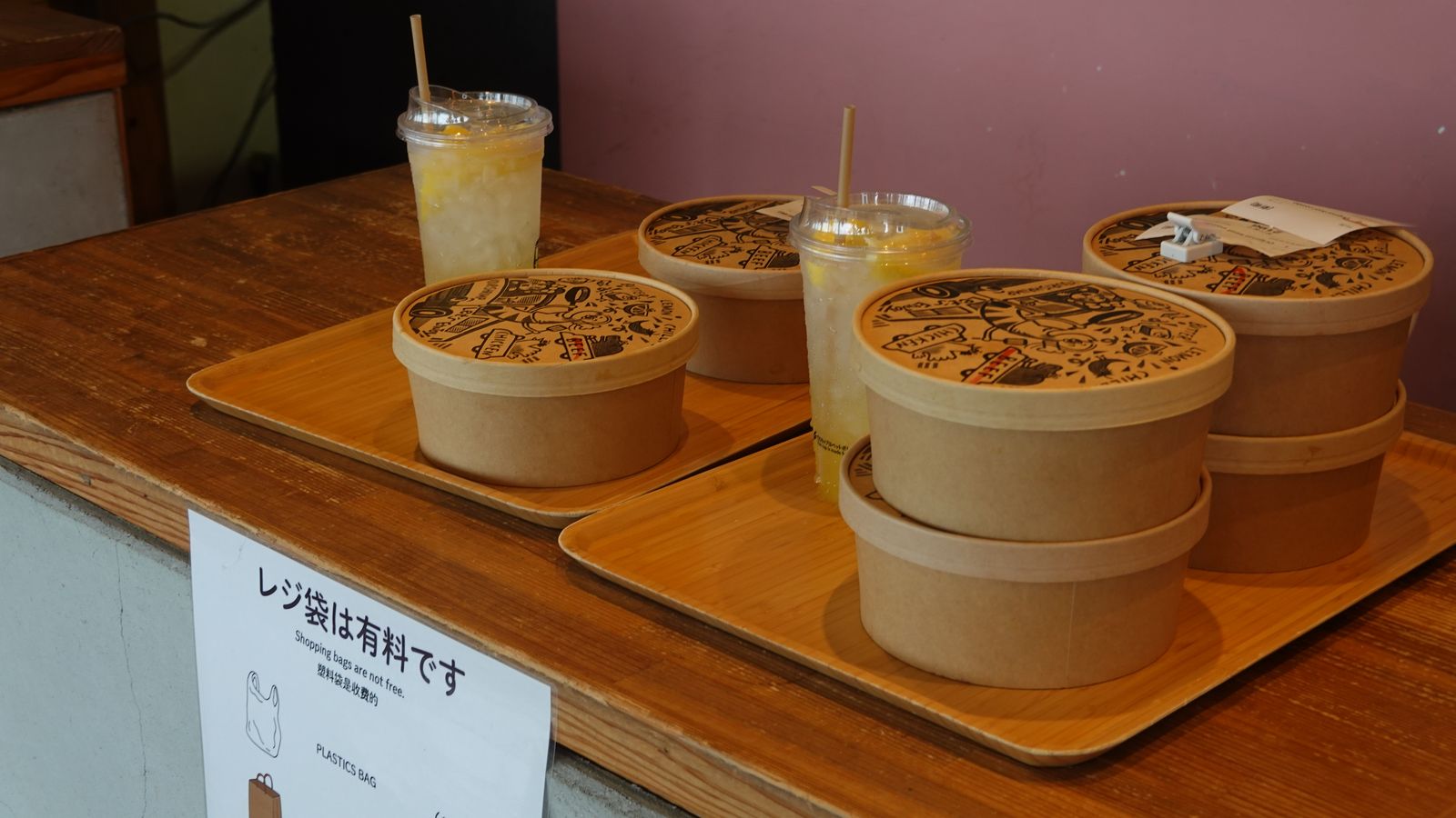 取餐櫃檯上用木托盤盛裝的蒜香蝦飯外帶餐盒與沖繩檸檬氣泡水飲料