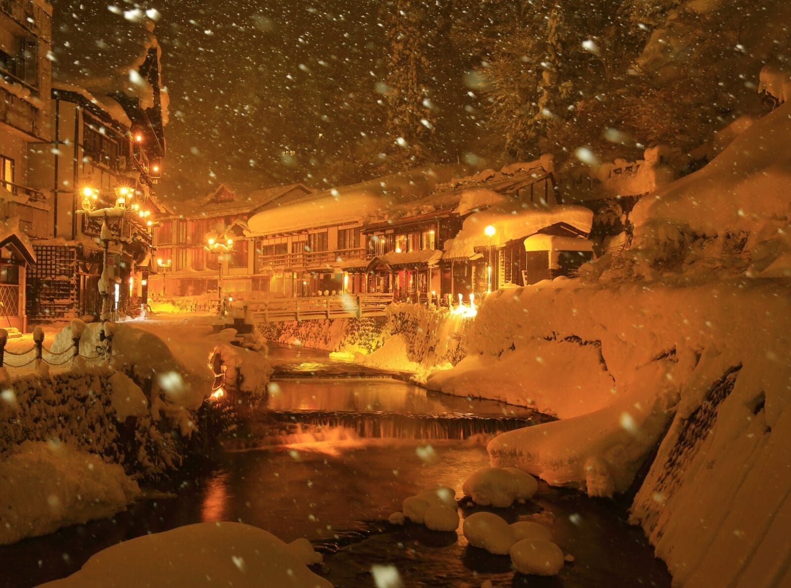 大雪紛飛時的銀山溫泉河岸、木造旅館與暖色燈光