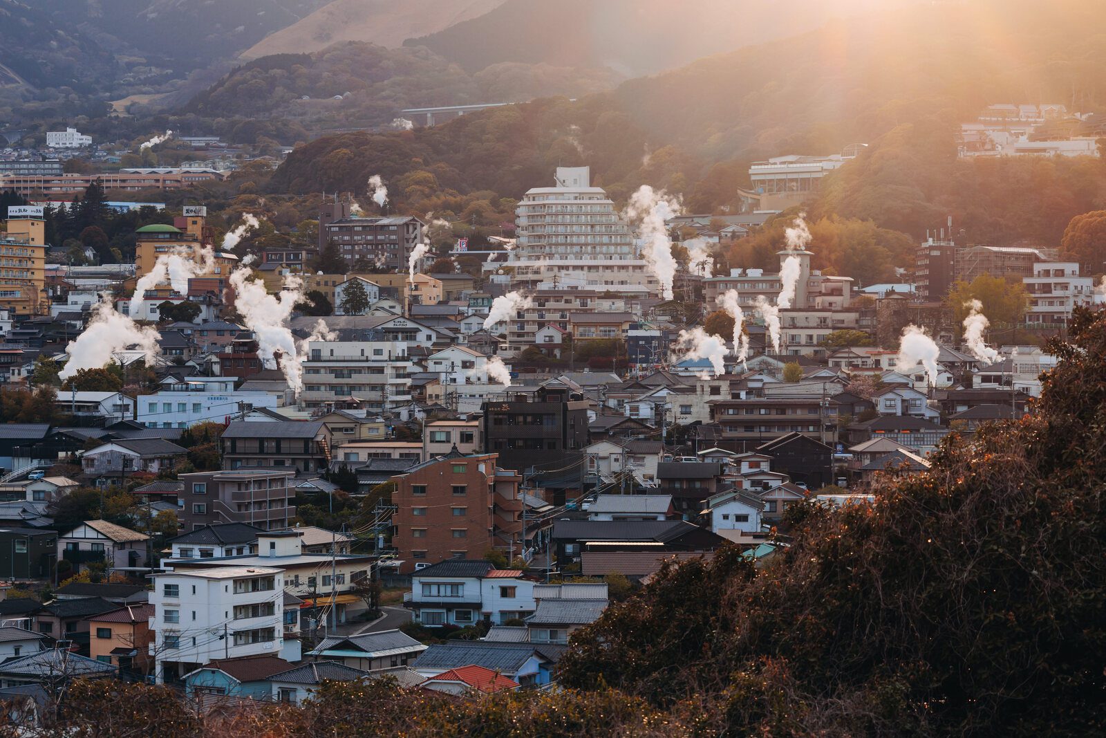 夕陽下的別府溫泉街，多處屋頂冒出白色湯煙