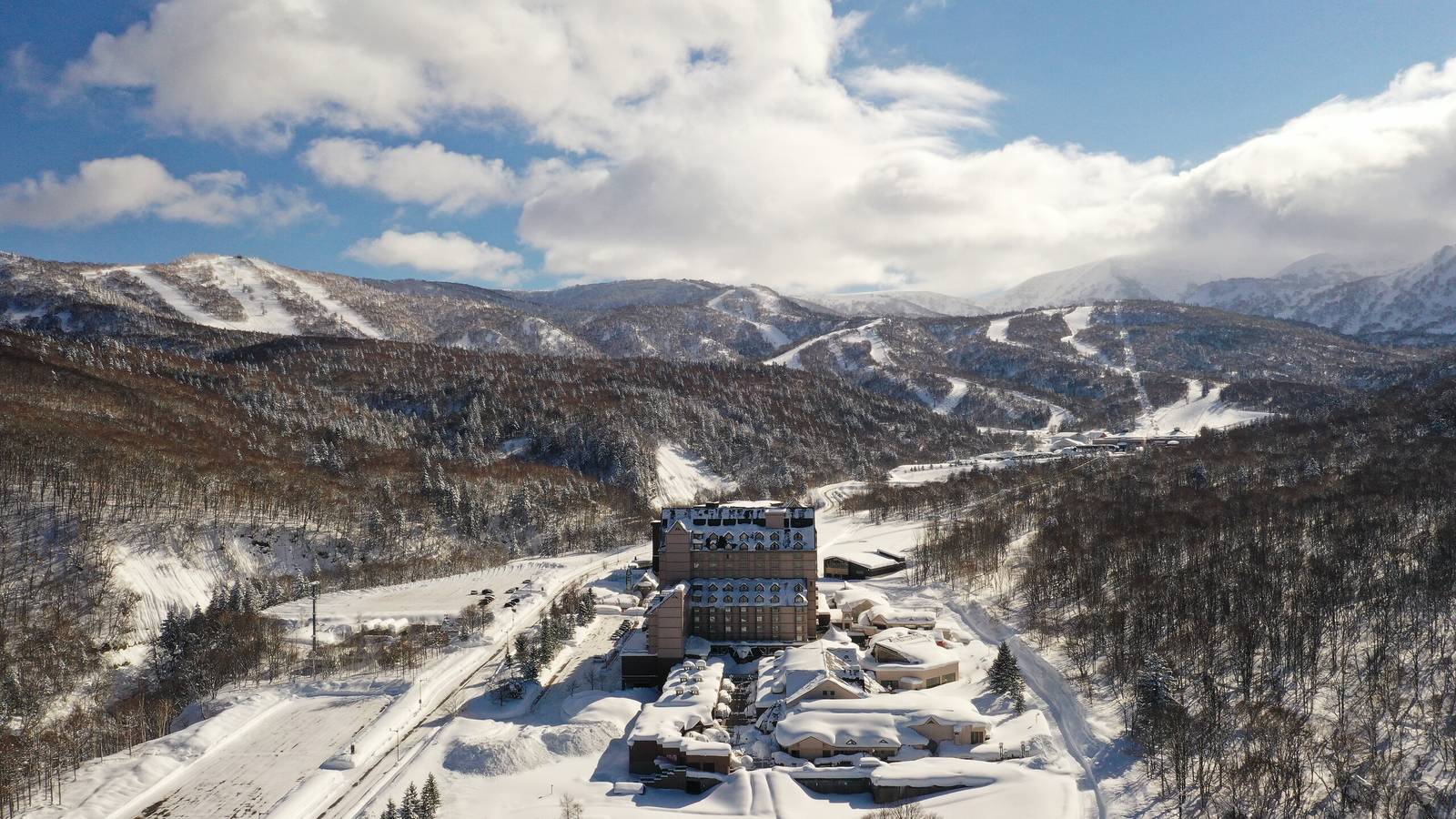 北海道喜樂樂 Grand 滑雪度假村｜冬季的喜樂樂雪場空拍，度假村建築群位於山谷雪道下方