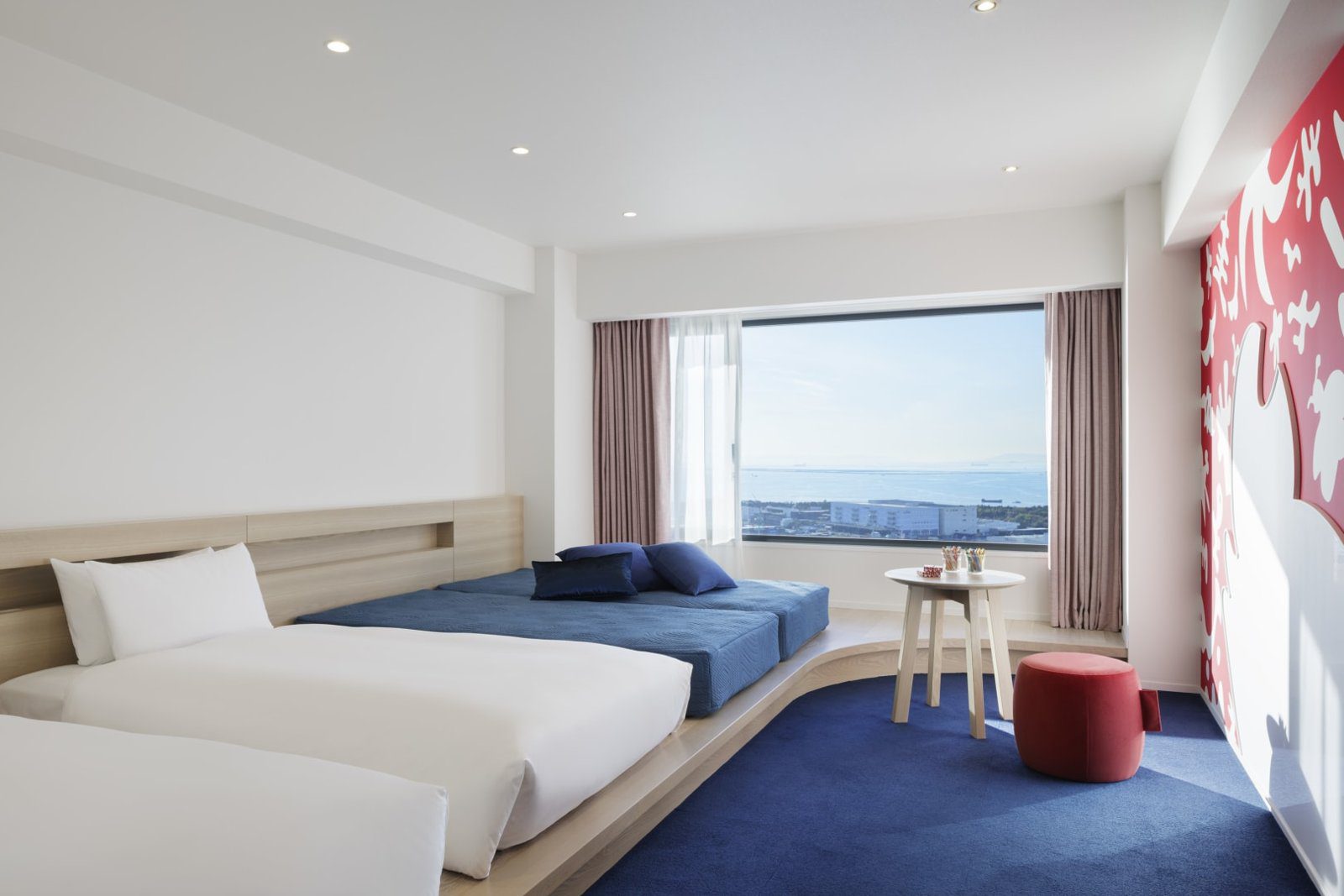 星野集團 RISONARE 大阪 Atelier Room 的床組、藍色臥榻與窗外港景